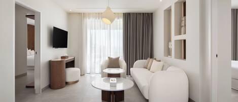 A modern hotel room with a sofa, a coffee table, a TV, and a large window with curtains.