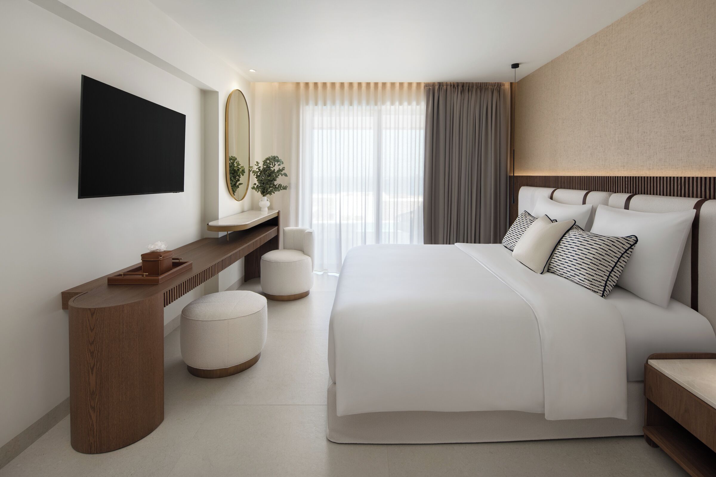 Ein modernes Hotelzimmer mit einem großen Bett, einem wandmontierten Flachbildfernseher, einem Holfnachtisch und einem großen Fenster mit durchsichtigen Vorhängen.