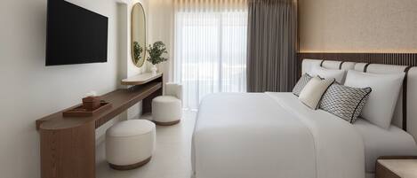 Une chambre d’hôtel moderne dotée d’un grand lit, d’un téléviseur à écran plat fixé au mur, d’une table de chevet en bois et d’une grande fenêtre ornée de rideaux légers.