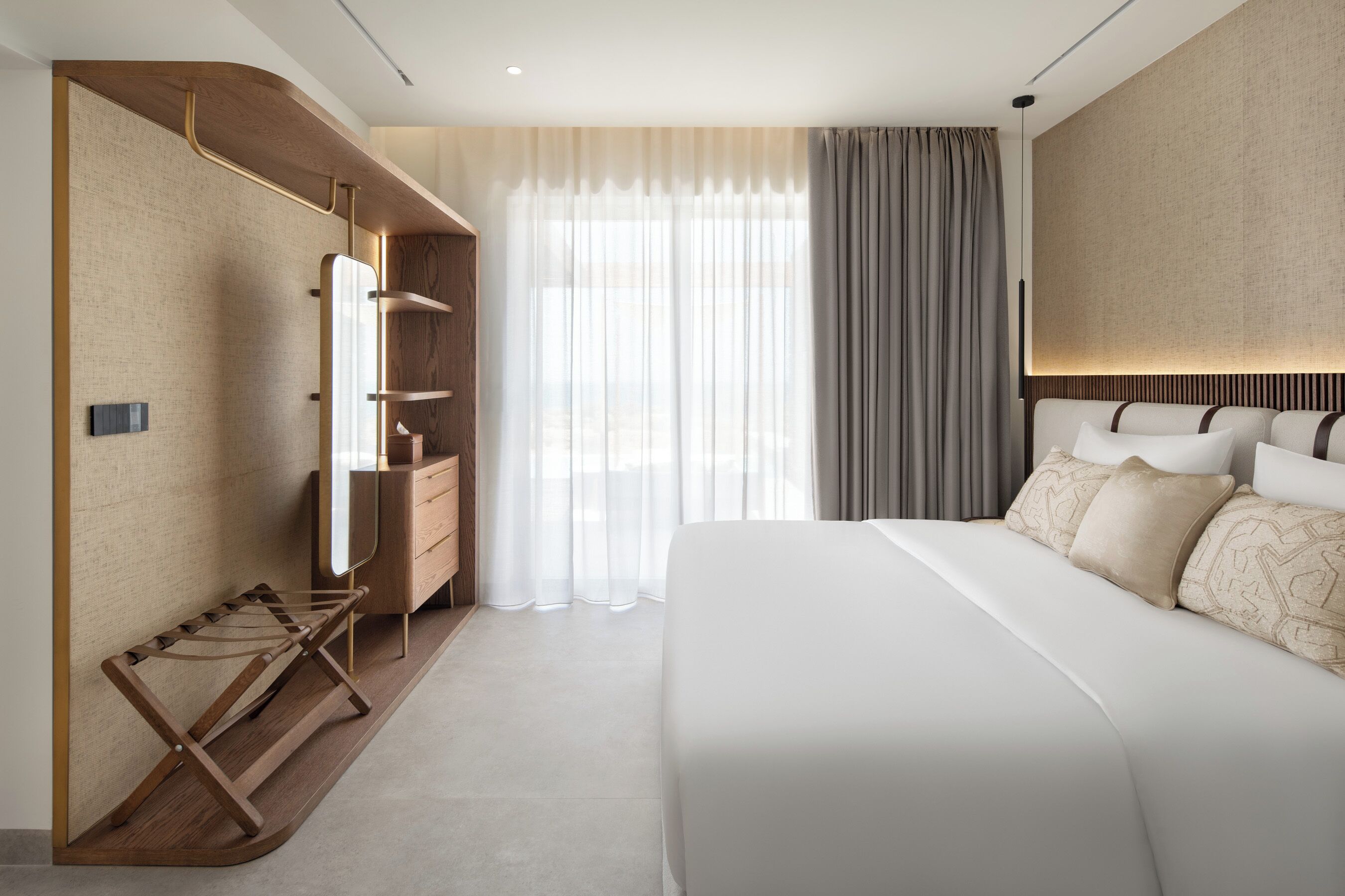 A modern hotel room with a large bed, a wooden wardrobe, a mirror, and a window with curtains.