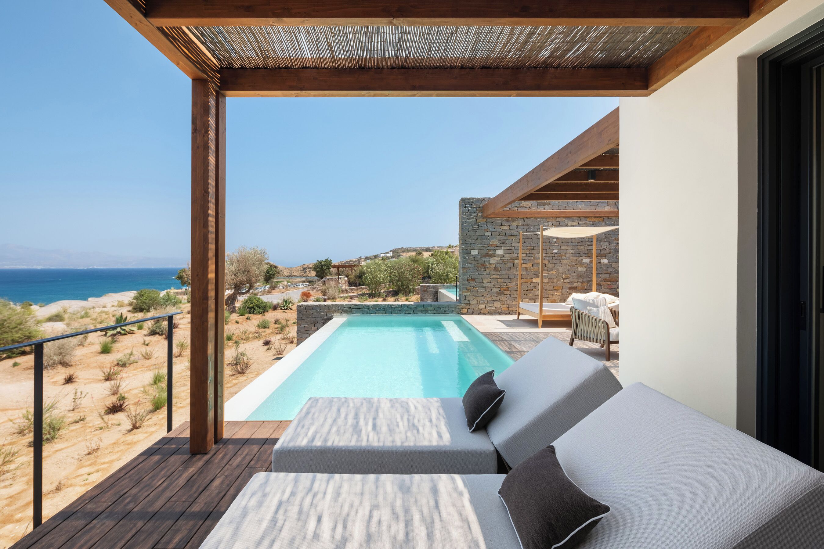 Un espace piscine extérieur moderne, doté d’une terrasse en bois, d’un mur en pierre et offrant une vue sur la mer.