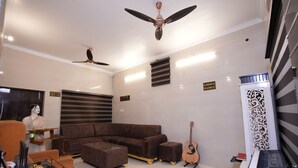 Una sala de estar moderna con un sofá seccional, una mesa de centro de vidrio, una mesita auxiliar, una guitarra, un teclado y un panel decorativo blanco.