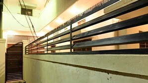 Un pasillo con barandilla metálica, una escalera y una puerta con reja de metal.