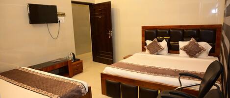 A hotel room with a bed, a desk, a chair, a TV mounted on the wall, and an air conditioning unit.
