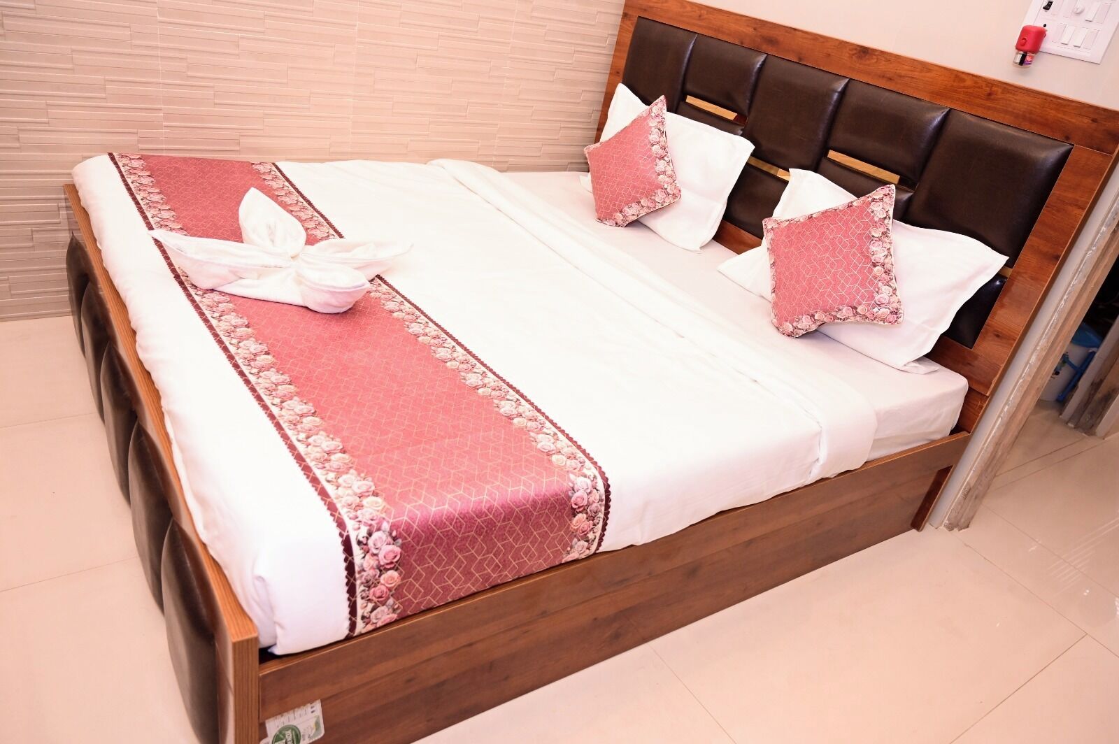 A neatly made bed with a wooden headboard, white bedding, and pink floral accents.
