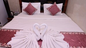 Habitación de hotel con cama, dos almohadas, una decoración de toallas con forma de corazón y una mesita de noche con hervidor.