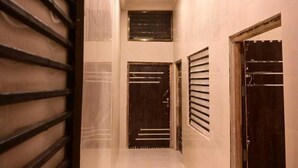 Un pasillo con piso brillante, barandilla metálica en un lado y puertas con barras horizontales.