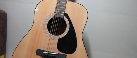 A classical acoustic guitar with a wooden body and a black pickguard, standing on a stand.