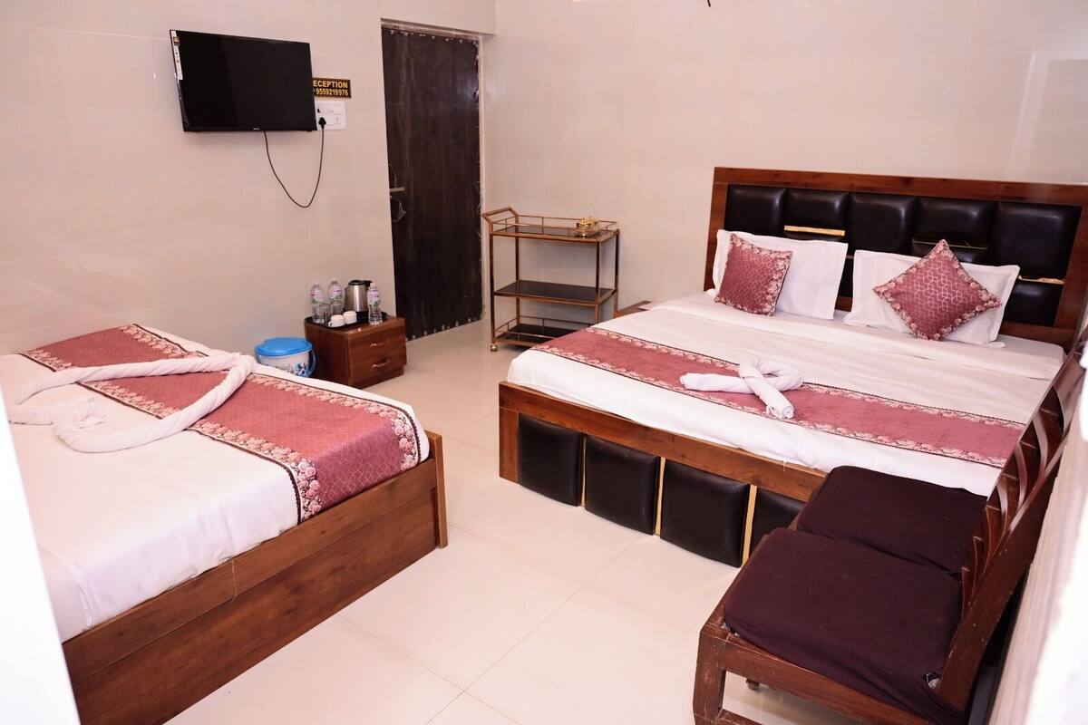 A hotel room with two single beds, a wooden headboard, a TV mounted on the wall, a small table with a tray, and a bench.