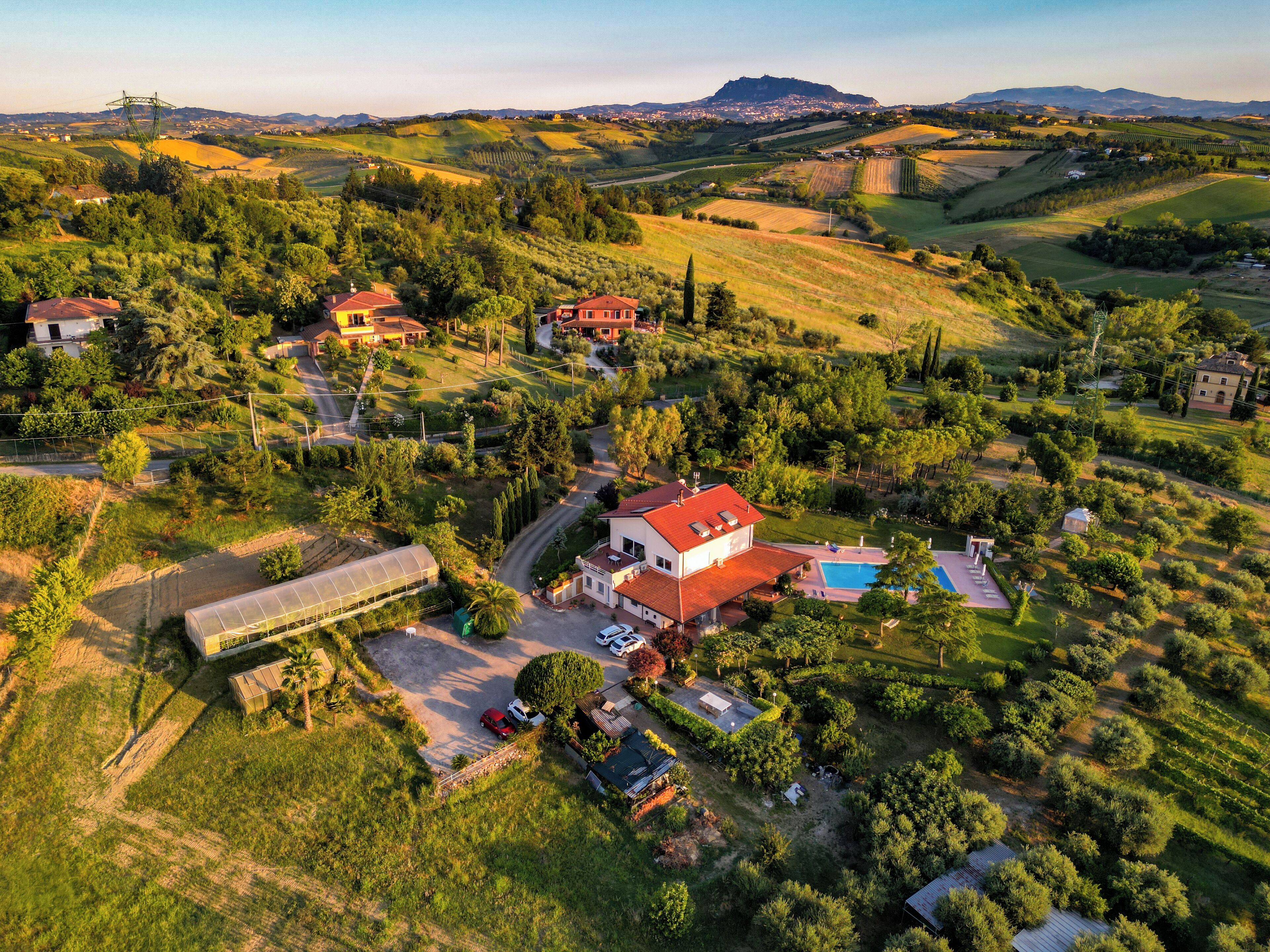 An aerial view of a rural property with multiple houses, a swimming pool, and surrounding green fields.