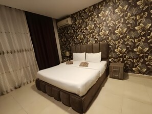 A neatly made bed with white linens and decorative pillows, a dark headboard, and a floral-patterned wall. - El RAYYAN HOTEL (Amman)
