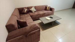 A modern living room with a brown sectional sofa, a glass coffee table, and a remote control on the table. - El RAYYAN HOTEL (Amman)
