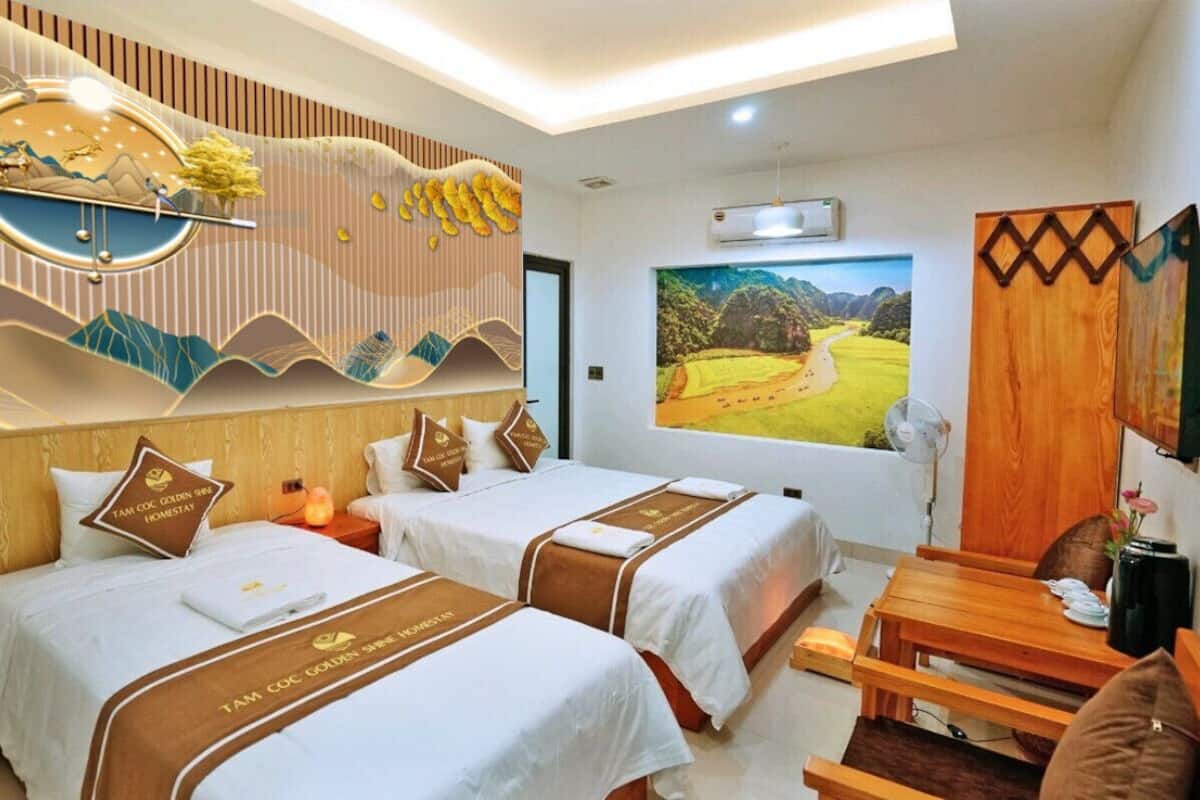 Ein Hotelzimmer mit zwei Betten, einem Holztisch, einem an der Wand befestigten Fernseher und einem großen Landschaftsbild.