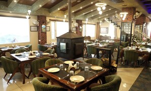 A restaurant with brick walls, patterned ceiling, and green upholstered chairs. Tables are set with plates, glasses, and cutlery. - The Hoften Al Shaykh Resorts, Srinagar (Srinagar)