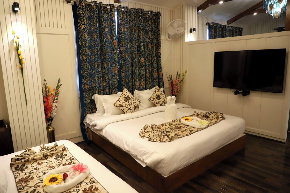 Quarto de hotel com uma cama grande, televisão de tela plana, um ventilador e cortinas decorativas.