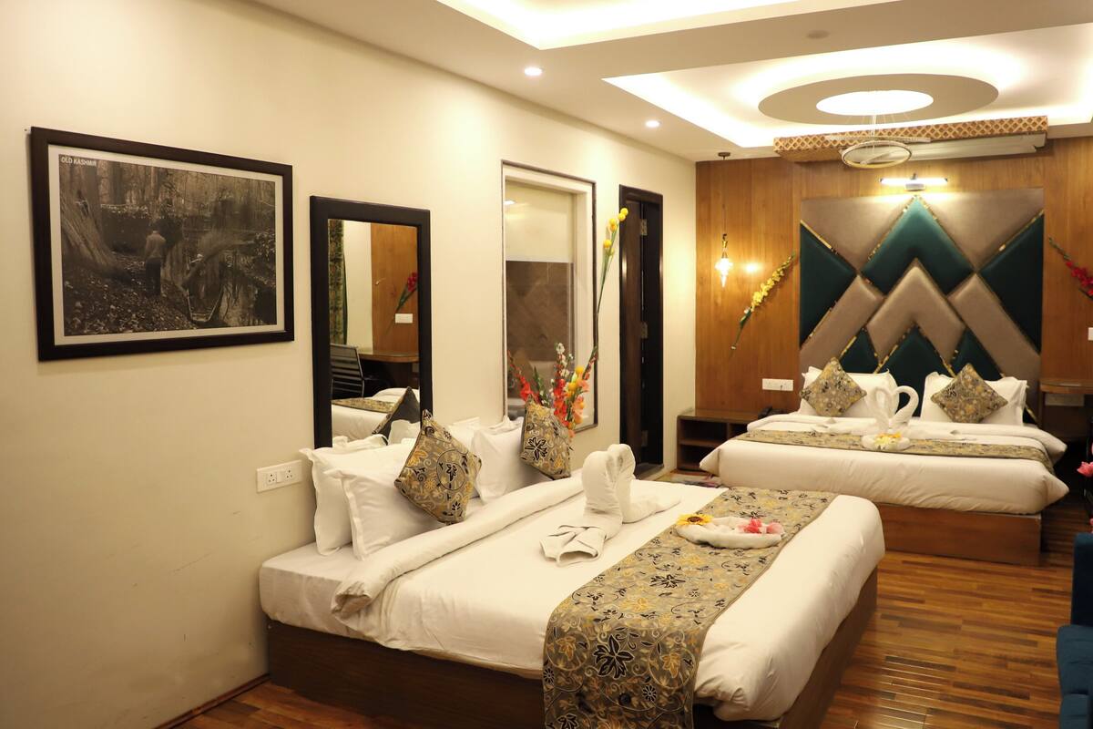 Quarto de hotel com duas camas, um espelho, um quadro emoldurado, uma parede decorativa e uma televisão.
