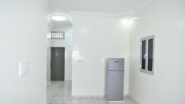 A hallway with white walls, a marble floor, a refrigerator, and a door leading to another room. - Socogim ps 41 (Nouakchott Ouest)