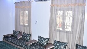 A room with a sofa set against a white wall, a window with a metal grill, and an air conditioning unit mounted above the window. - Socogim ps 41 (Nouakchott Ouest)
