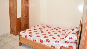 A bedroom with a bed covered in a strawberry-patterned bedspread, a wooden wardrobe, and a tiled floor. - Socogim ps 41 (Nouakchott Ouest)