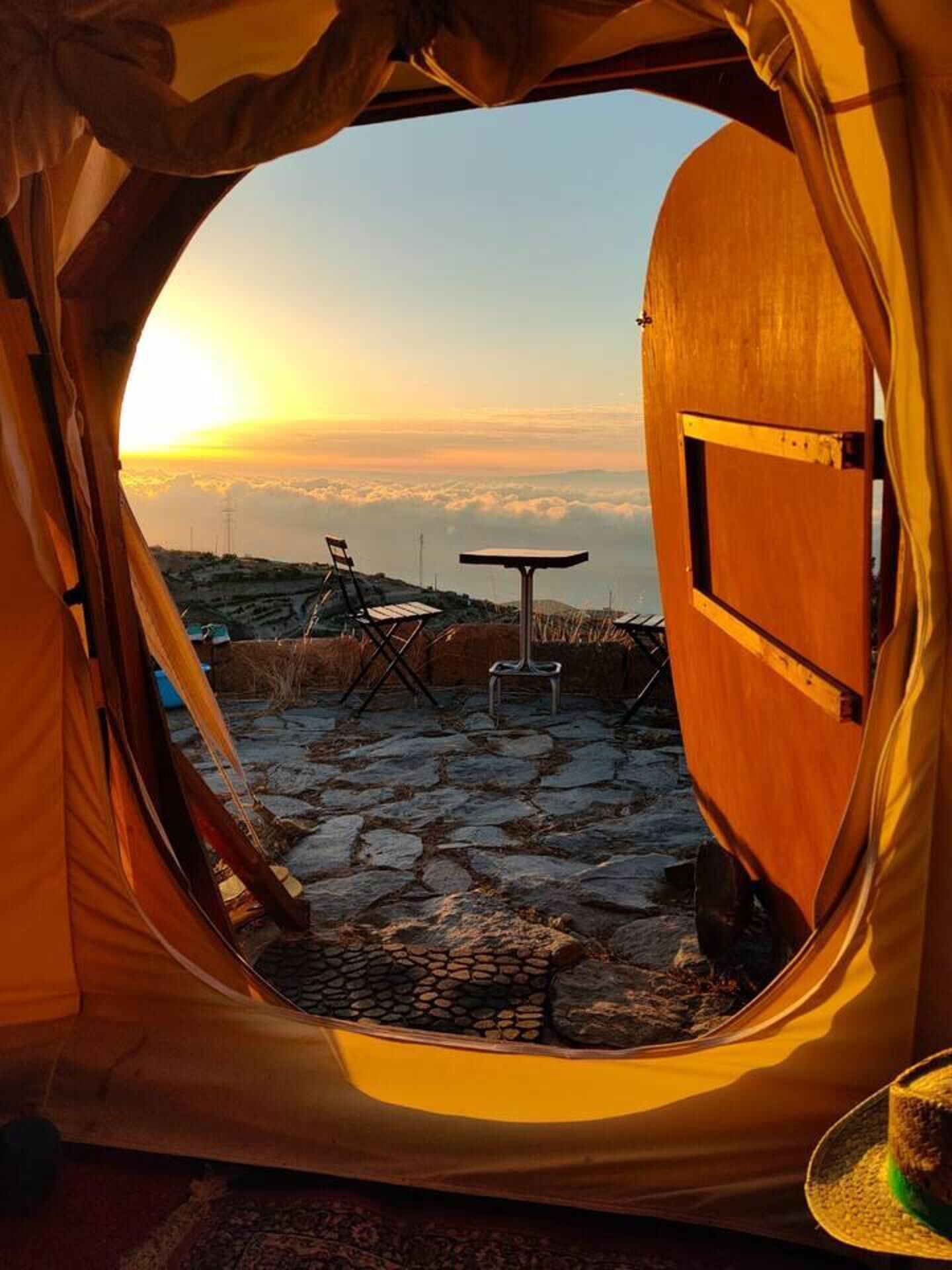 A tent with a view of a stone patio, a table, and chairs.