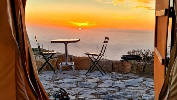Ein Zelt mit Blick auf einen Sonnenuntergang über einem felsigen Strand, einem Tisch und zwei Stühlen.