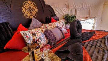 Una cama con cabecera, almohadas, una manta, una botella de vino y una copa.