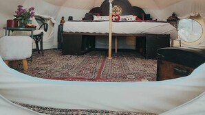 Ein gemütliches Zelt mit Bett, einem kleinen Tisch und einer Blumenvase sowie einem Teppich.