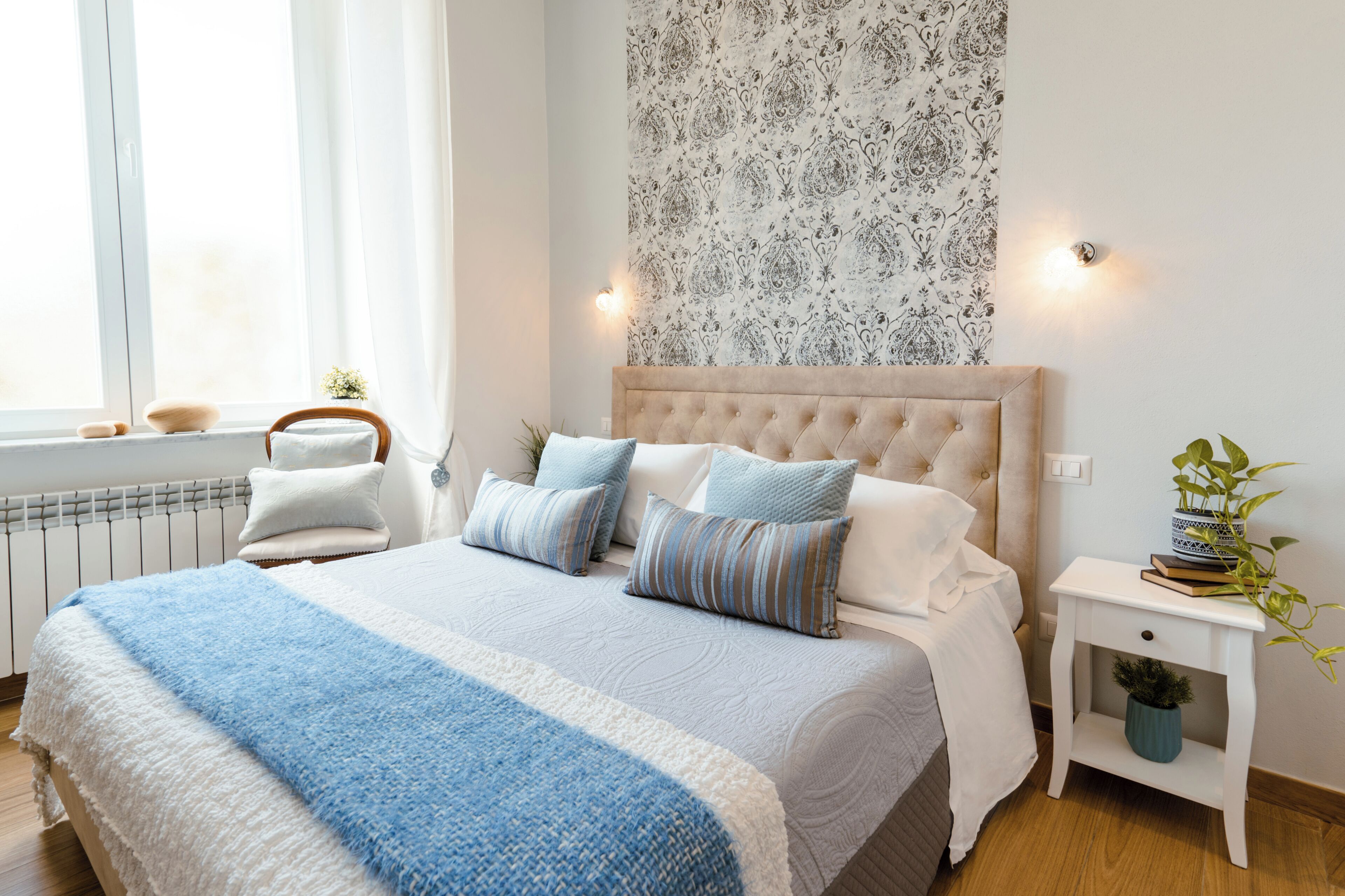 Un dormitorio con una cama grande, una mesita de noche con una planta y una ventana con cortinas.
