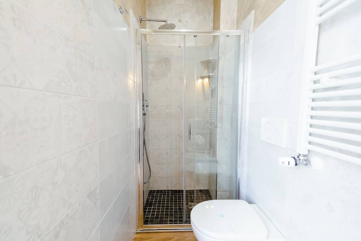 Une salle de bain moderne avec une douche à parois de verre, des toilettes blanches et un sol carrelé.