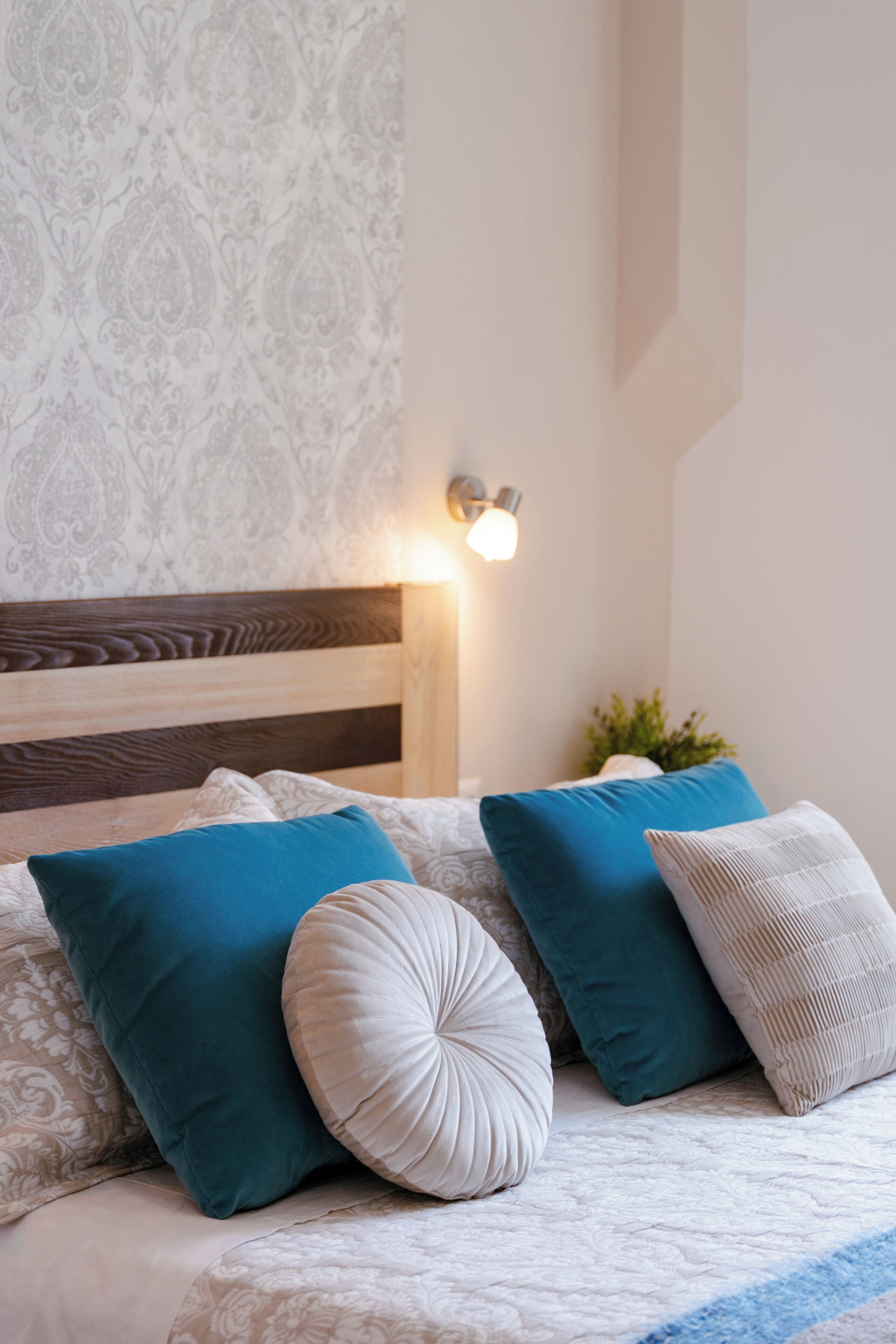 Een slaapkamer met een houten hoofdbord, behang met een patroon en een bedlampje.