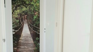 Käytävän lattia on tehty puusta, ja se johtaa ovelle, jossa on kuva metsästä ja sillasta.
