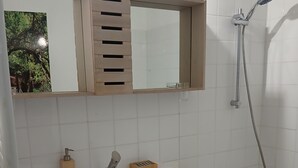 Kylpyhuone, jossa on puinen allaskaappi, peili, pesuallas, suihku ja kylpyamme.