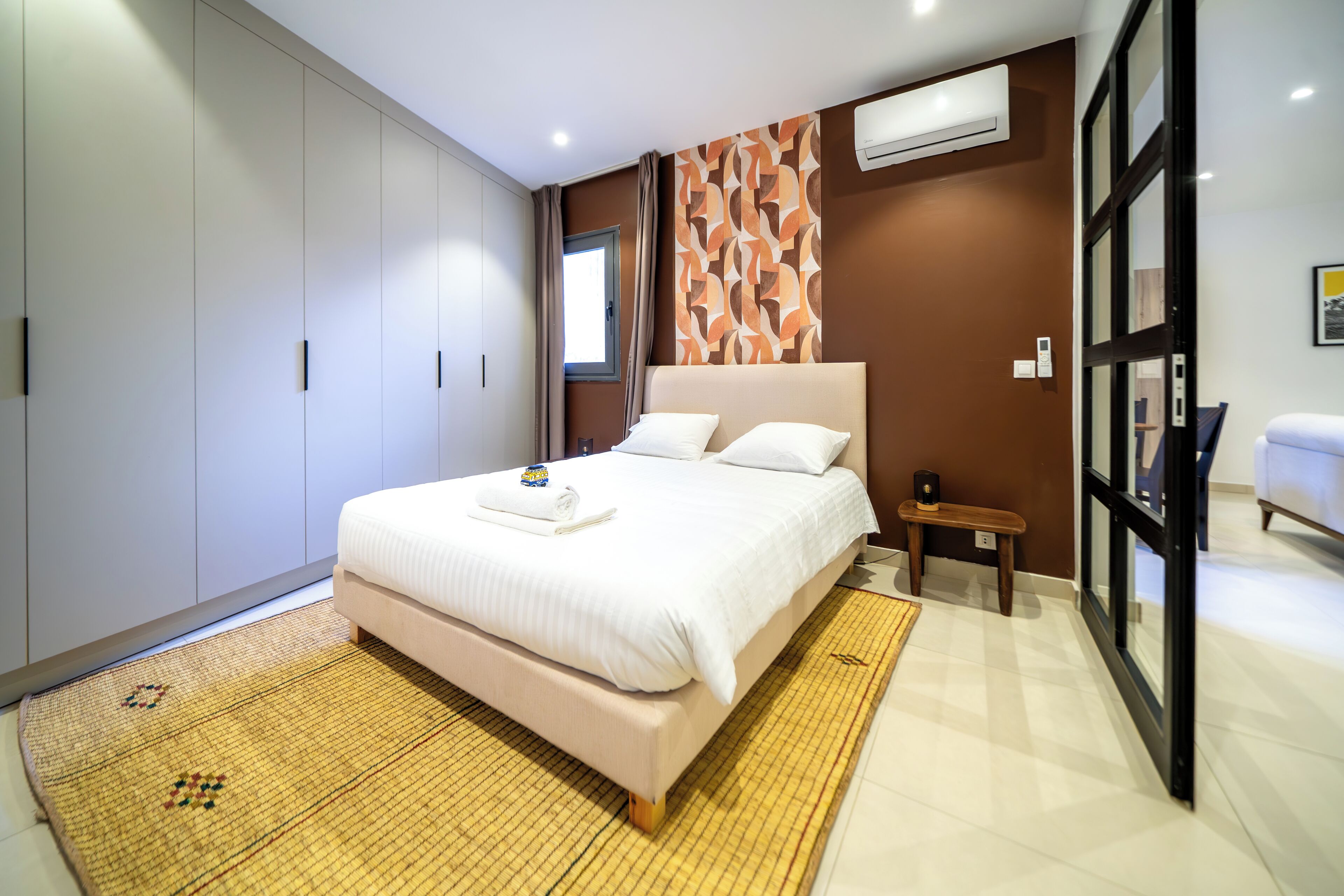 A modern bedroom with a large bed, a wardrobe, and a small bedside table.