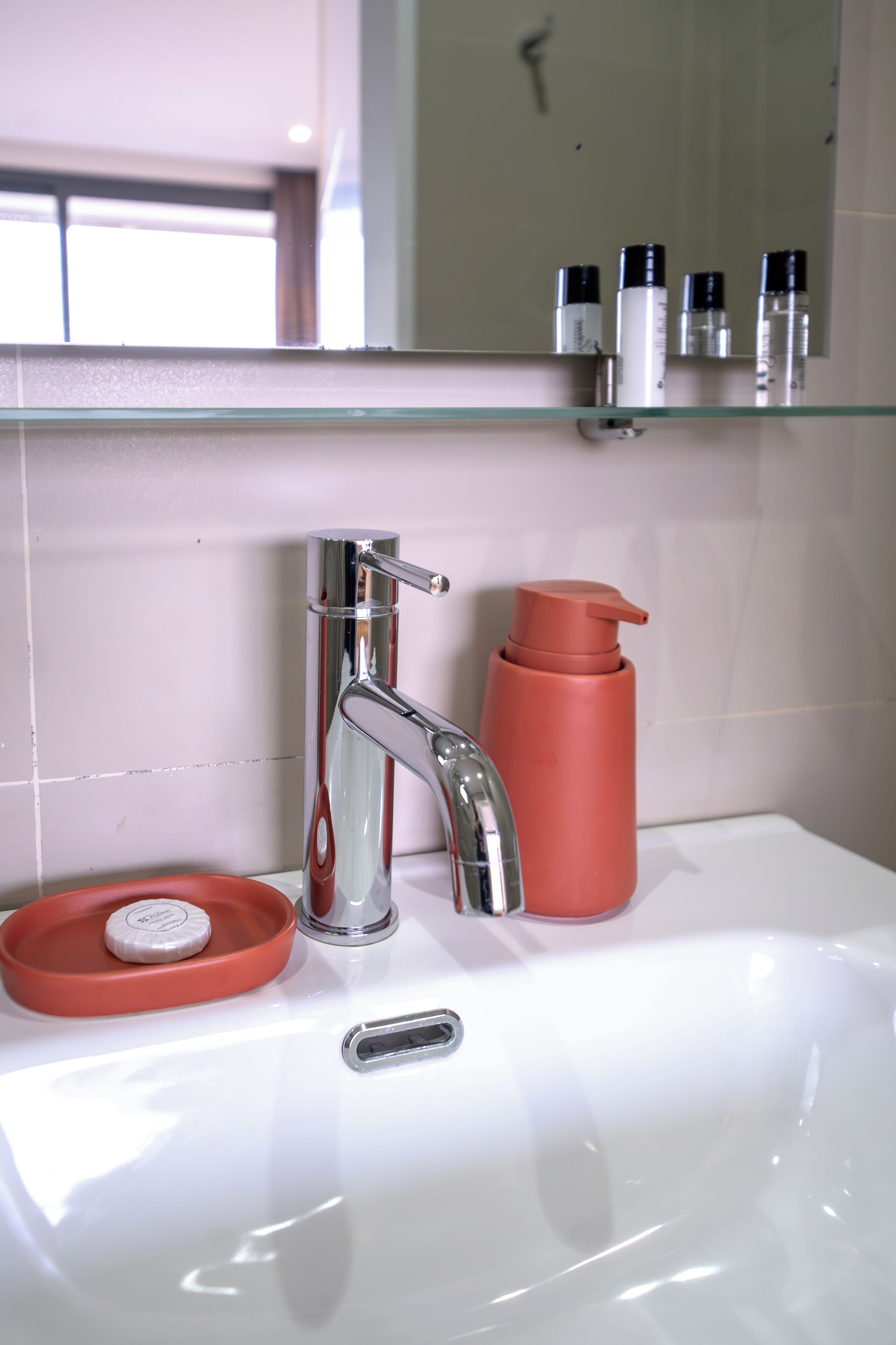 A bathroom with a white sink, chrome faucet, and a red soap dish.