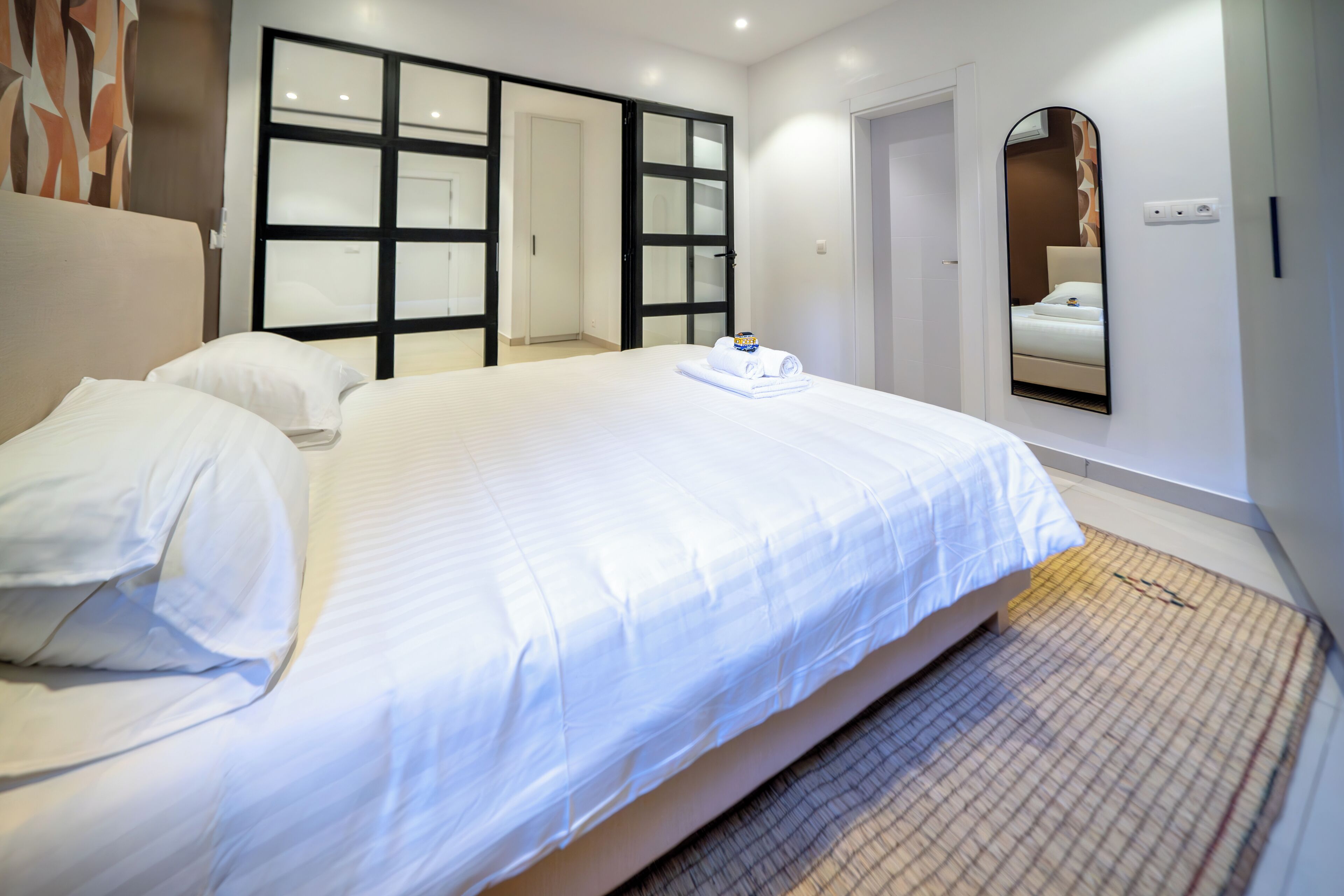 Une chambre d’hôtel avec un grand lit, une armoire aux portes vitrées, un miroir et un tapis à motifs.
