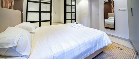 A hotel room with a large bed, a wardrobe with glass doors, a mirror, and a patterned rug.