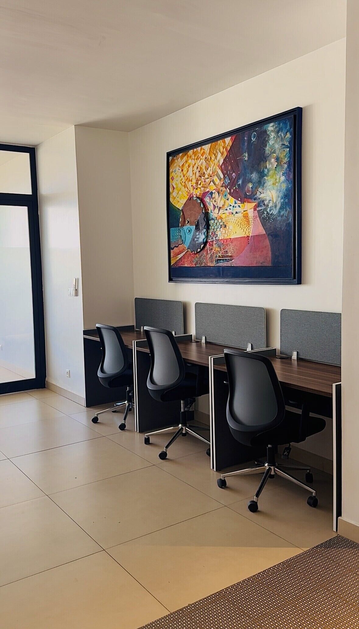 A conference room with four black office chairs, a long table, and a colorful abstract painting on the wall.