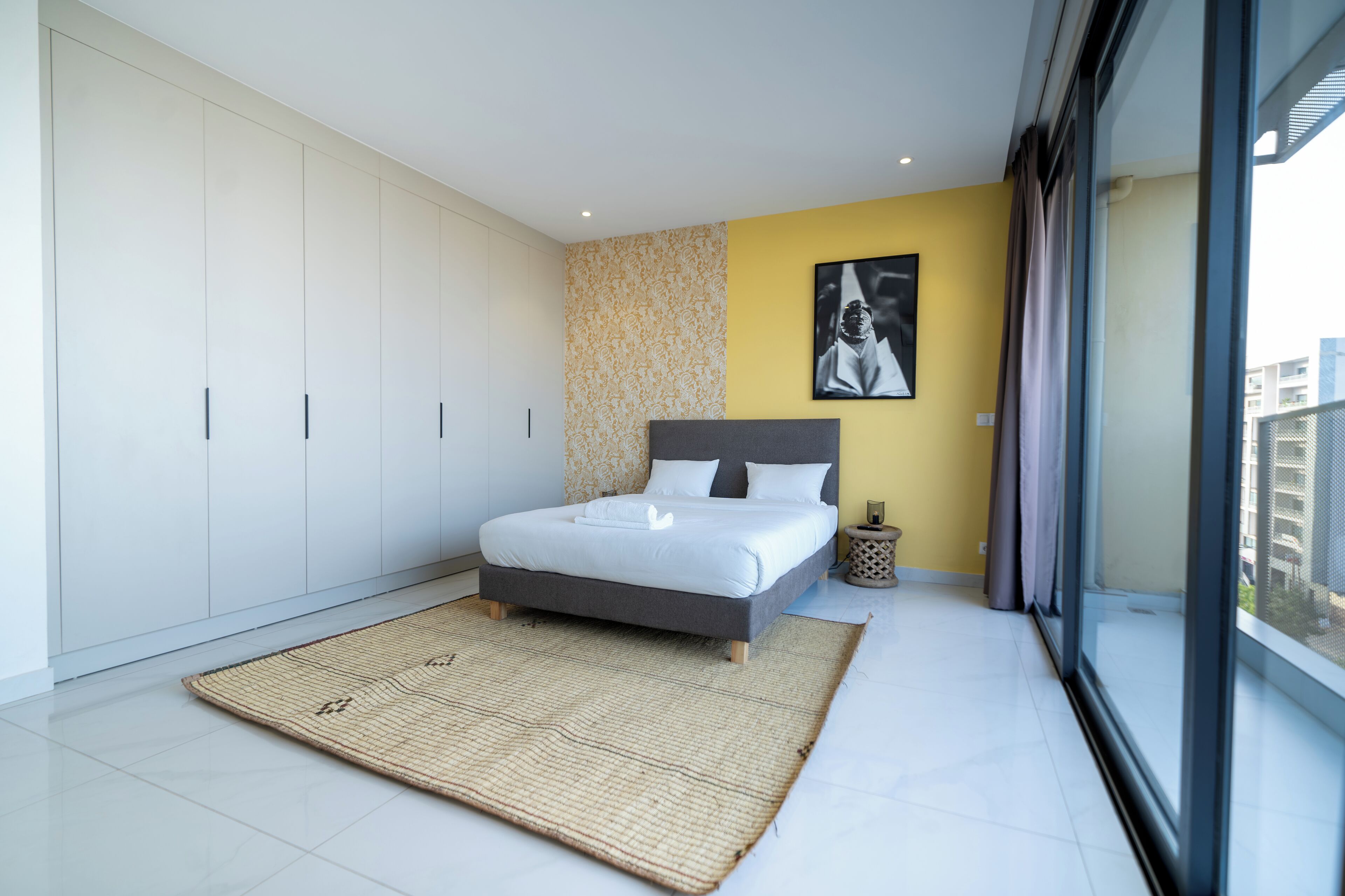Une chambre moderne avec un grand lit, une vue sur la ville grâce à une grande fenêtre et un design minimaliste.