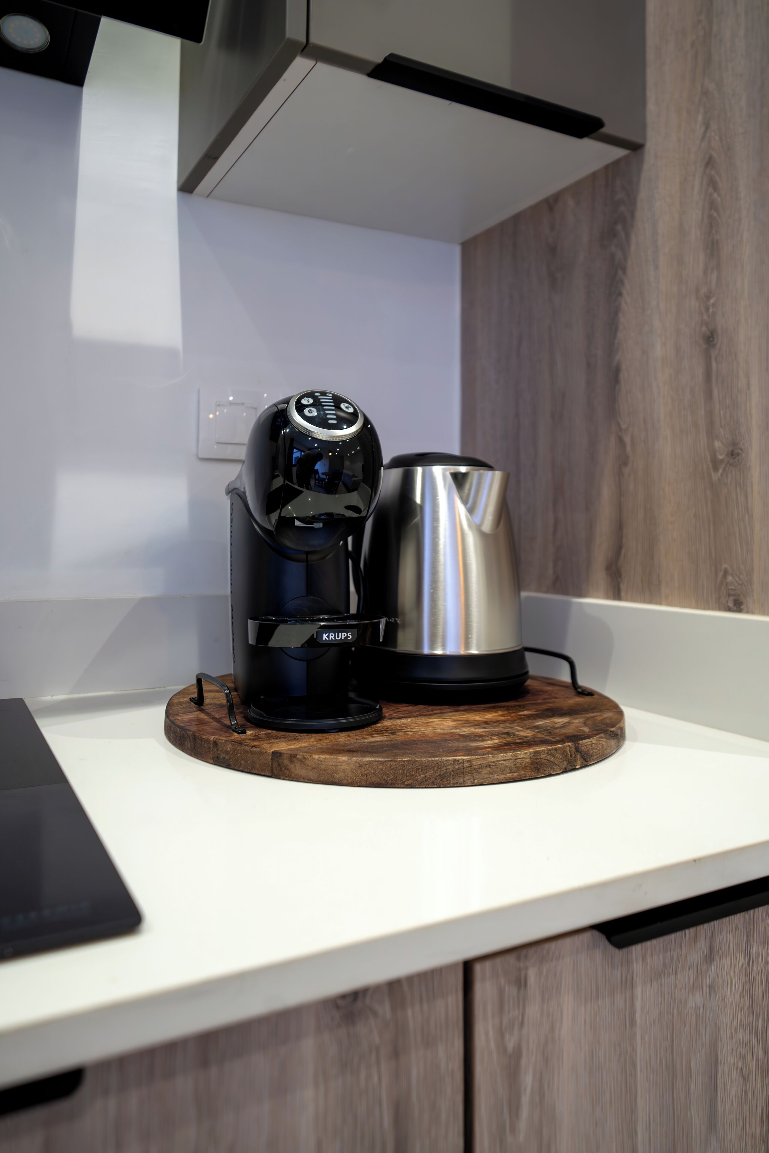 Una cocina moderna con una cafetera y un hervidor sobre un posavasos de madera.