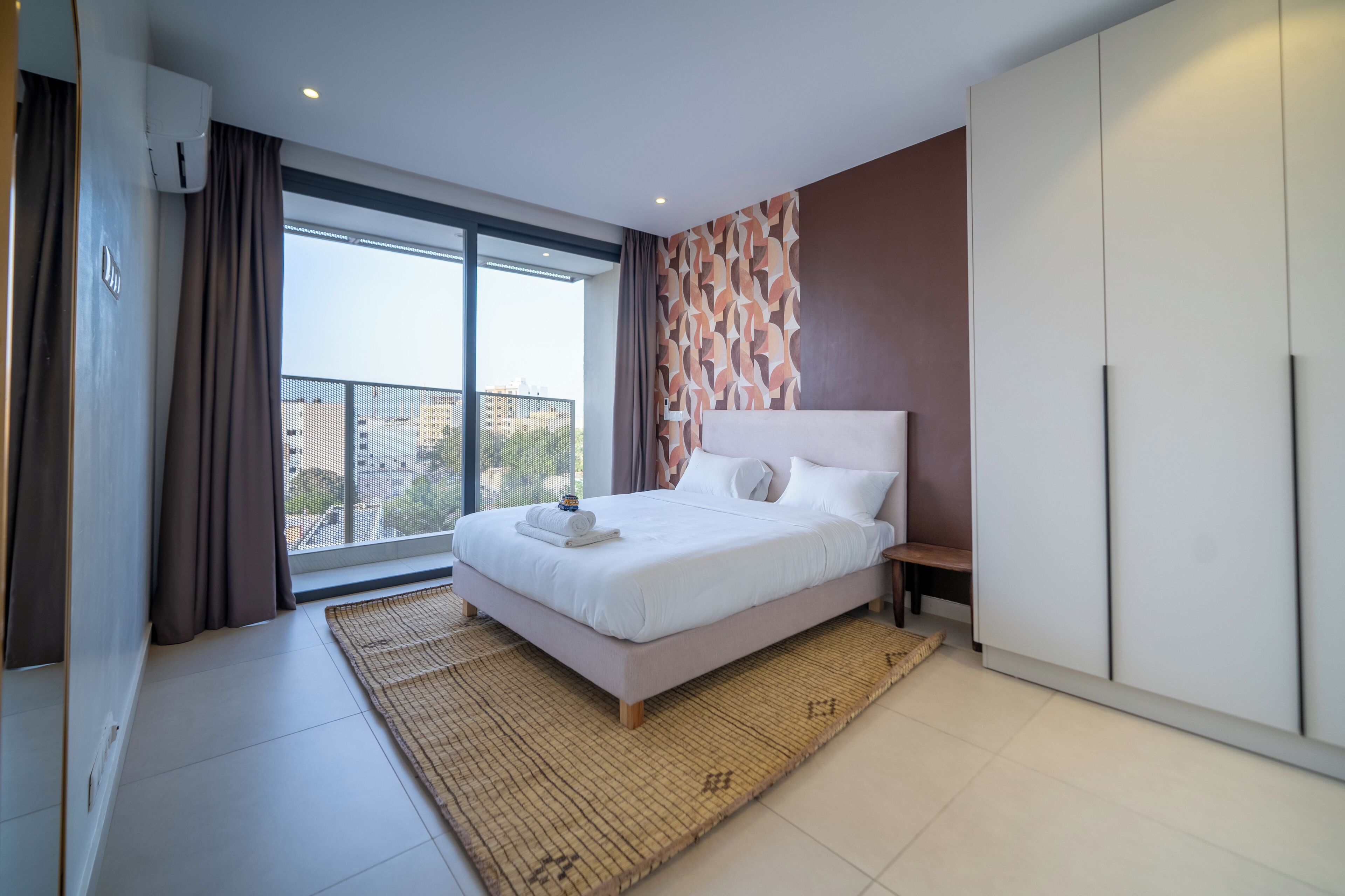 A modern hotel room with a large bed, a view of the city, and a balcony.