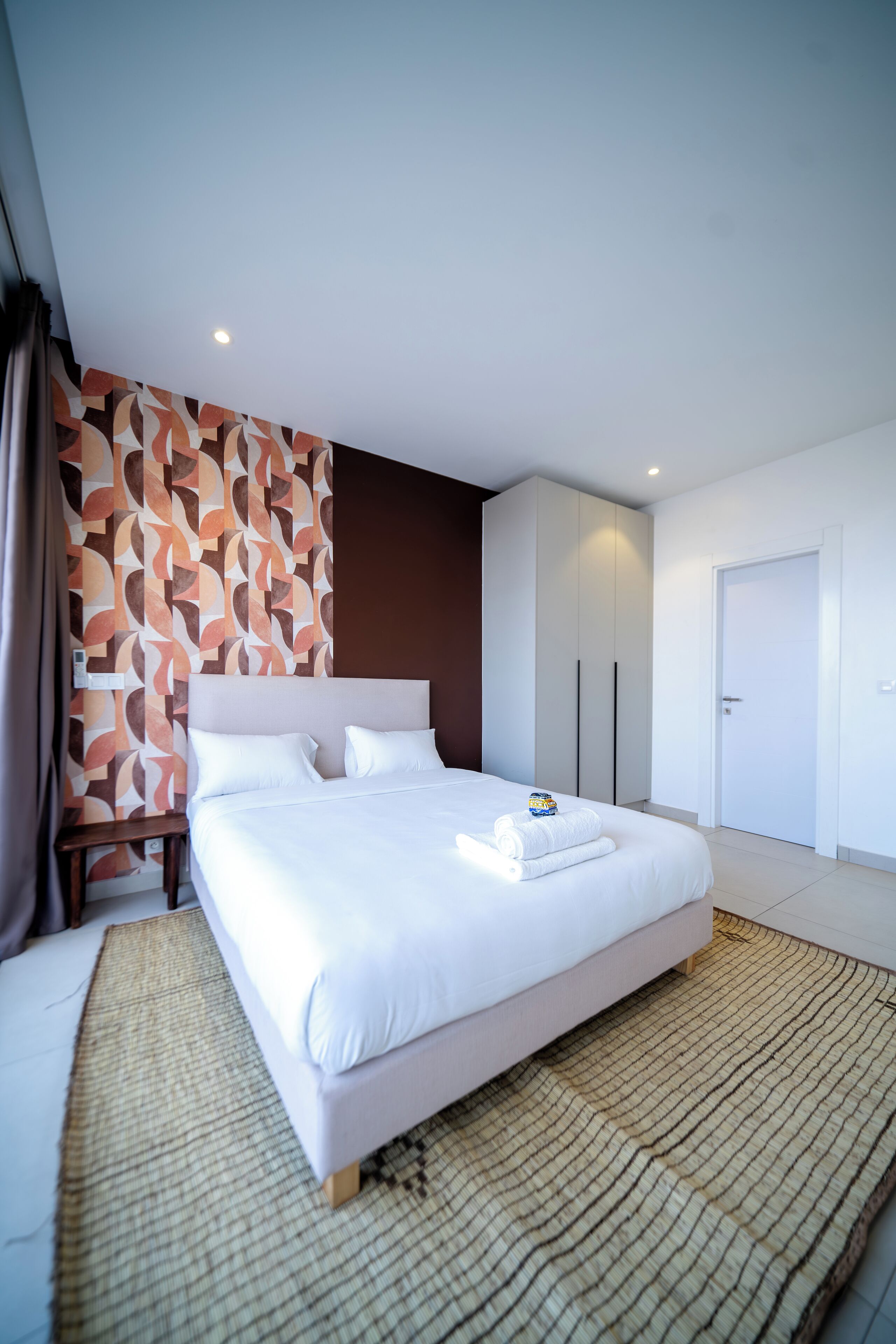 A modern hotel room with a large bed, a bedside table, and a patterned wall.
