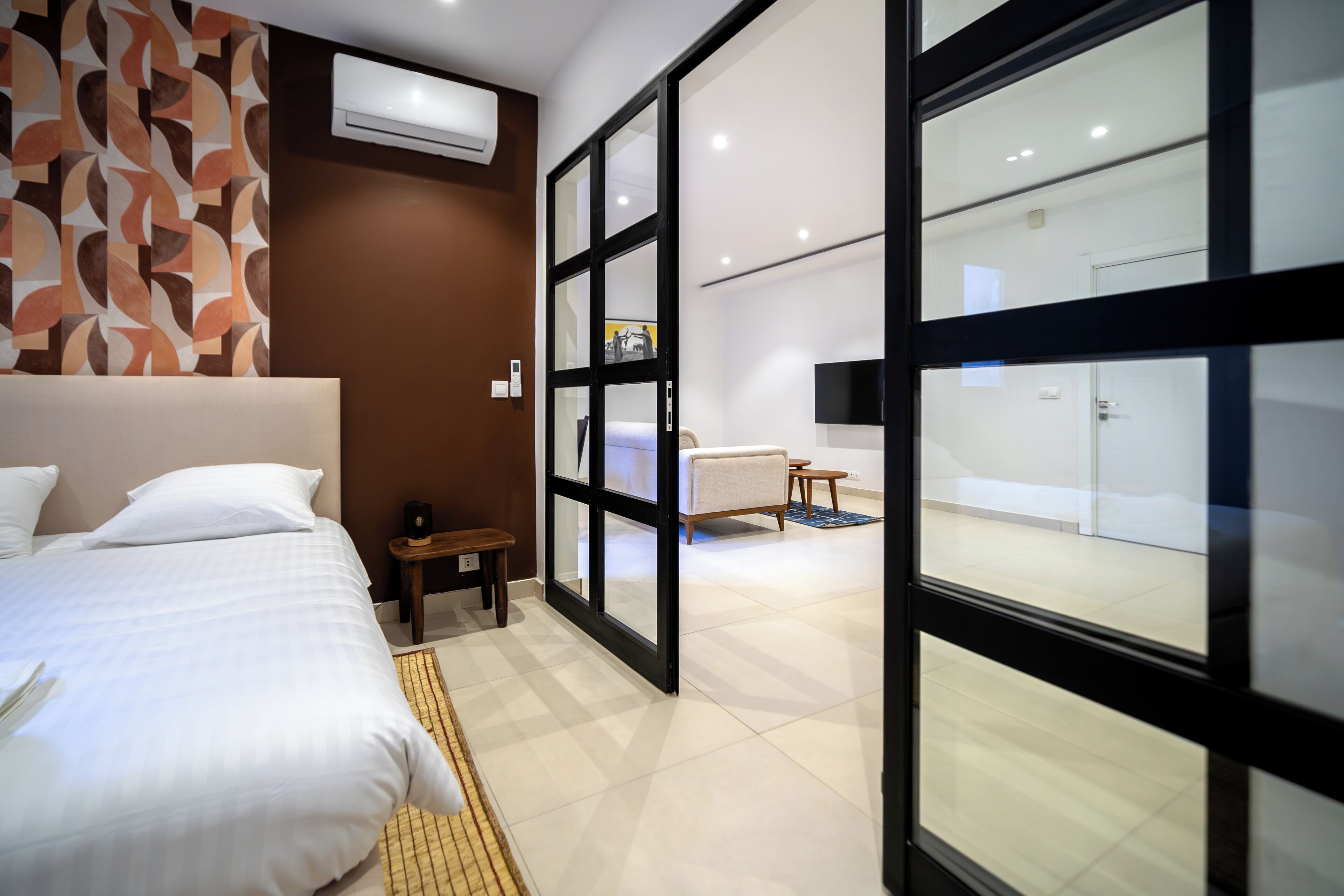 A modern hotel room with a large bed, a small bedside table, a chair, and a view through a glass door to a bathroom.