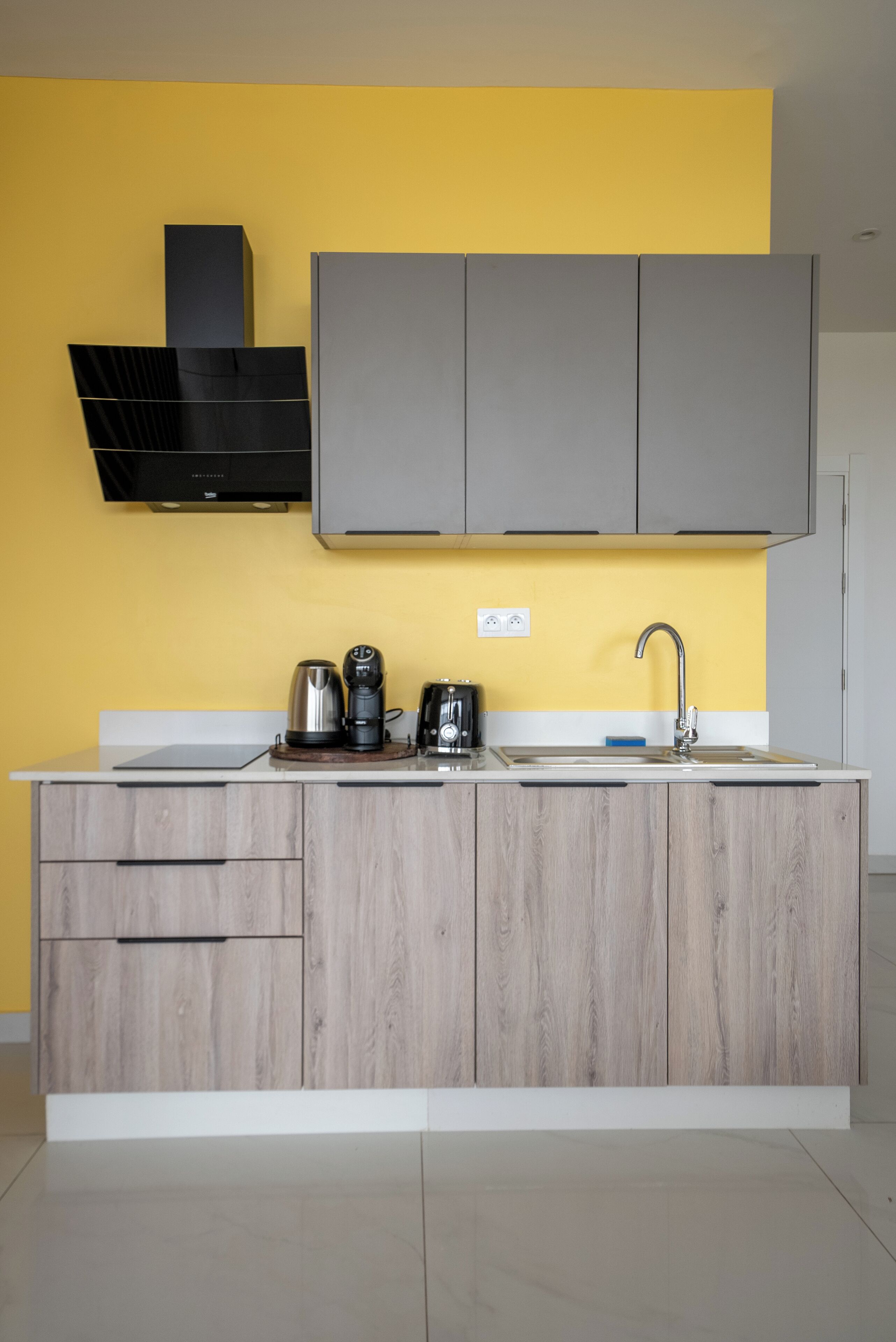 A modern kitchen with a yellow wall, grey cabinets, and a white countertop.