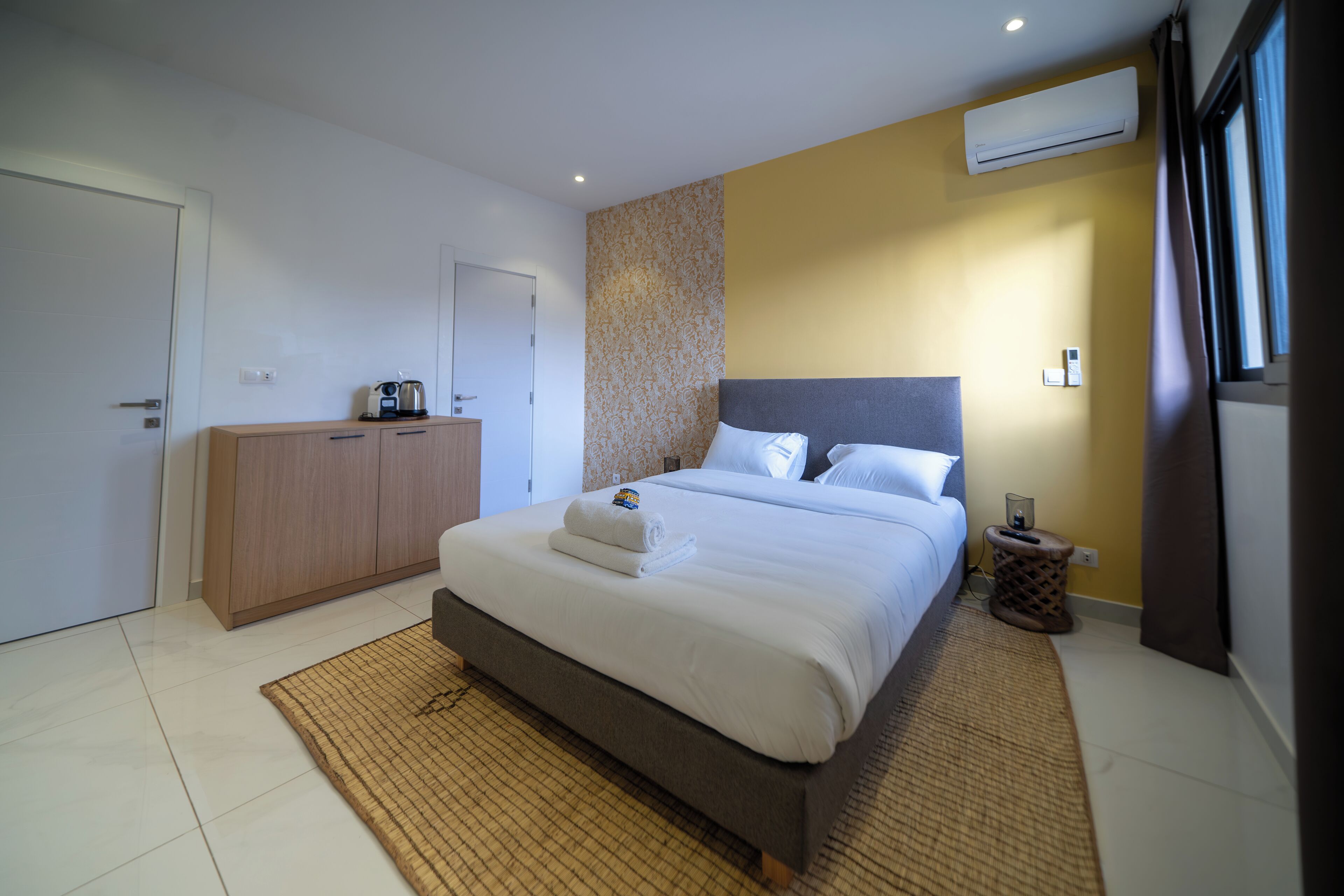 Una habitación de hotel moderna con una cama grande, un armario de madera y una mesita de noche pequeña.