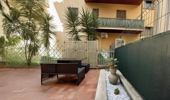 Une terrasse extérieure avec une table en bois et des bancs, entourée d’une petite clôture et de plantes en pot.