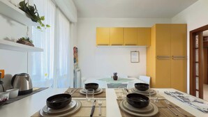 A dining area with a table set for four, including bowls, plates, cutlery, and glasses. There are yellow cabinets above the table and a plant on the wall. - Casa Cartesio, steps from San Siro & Ippodromo (Milano)