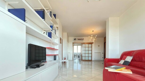 A modern living room with a flat-screen TV, white shelves, a red sofa, and a tiled floor. - Casa Cartesio, steps from San Siro & Ippodromo (Milano)