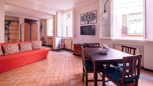 Una habitación con un sofá rojo, una mesa de comedor de madera, sillas, un televisor y una ventana con persianas.
