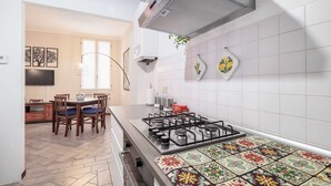Una cocina con estufa a gas, salpicadero de azulejos blancos y una zona de comedor con mesa y sillas.
