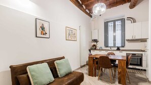 Una sala acogedora con un sofá de cuero marrón, una mesa de comedor de madera y una cocina con armarios blancos y una ventana.